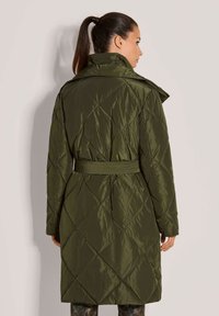 Olijfgroene gewatteerde parka met een ceintuur in de taille, hoge kraag en lange mouwen. Heeft diamanten patronen op de stof en een gladde textuur.