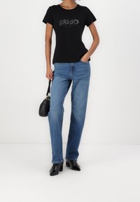 Czarny t-shirt z krótkim rękawem z błyszczącym logo "LIUJO MILANO", zestawiony z jasnoniebieskimi jeansami o prostym kroju i czarnymi szpilkami.