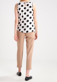 Débardeur blanc sans manches avec de grands pois noirs, pantalon beige ajusté et ballerines noires. Détail en trou de serrure au dos du débardeur.