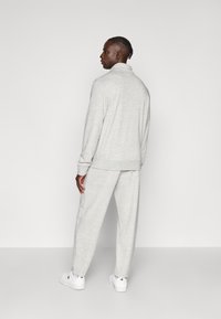 Γκρι φούτερ και αντίστοιχο παντελόνι φόρμας, και τα δύο με μαλακή υφή. Διαθέτουν ριμπ μανσέτες και γιακά που στέκεται όρθιος. Άσπρα αθλητικά παπούτσια ολοκληρώνουν την εμφάνιση.