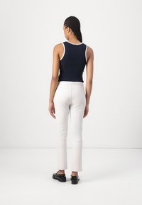 Mörkblå ribbad linne med vit kant, kombinerat med krämfärgade tajta byxor och svarta platta skor. Bakifrån visad outfit.
