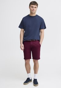 T-shirt en coton navy à manches courtes, associé à un short en coton bordeaux. Le modèle porte des chaussettes blanches et des baskets navy avec une semelle texturée.