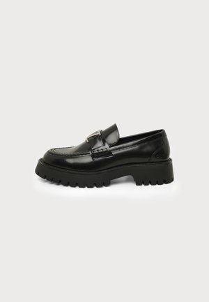 Black leather loafer with chunky lug sole and metal buckle detail, side view on a light background.