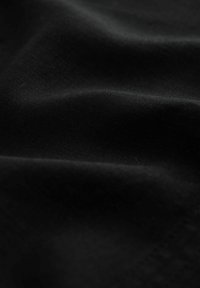 Tissu noir à la texture lisse, présentant une légère brillance et de douces plis, créant un motif dynamique évoquant des vagues.