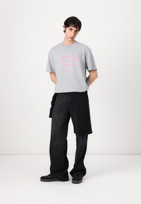 Grå bomulls t-skjorte med rød "TOMMY JEANS NEW YORK" logo, kombinert med svarte denimbukser, som har en avslappet passform og uformell stil.