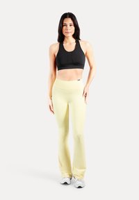 Schwarzes Sport-BH mit Rundhalsausschnitt, kombiniert mit hellgelben Schlagleggings. Beide Kleidungsstücke sind enganliegend und aus elastischem Material gefertigt.