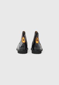 Bottines en cuir noir avec une finition brillante, bout rond et semelle en caoutchouc texturé. Présente une étiquette orange avec un emblème au talon.
