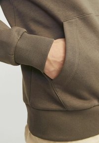 Bruine katoenen hoodie met een voorzak en geribde manchetten. De stof heeft een gladde textuur met contrasterende geribde onderrand en mouwaccenten.