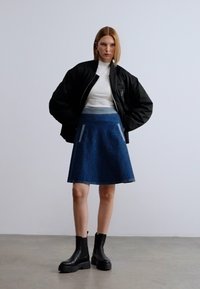 Μαύρο μπουφάν μπόμπερ, λευκό ζιβάγκο, μπλε τζιν φούστα σε γραμμή Α με γκρι λεπτομέρειες και μαύρες μποτάκια μέχρι τον αστράγαλο με χοντρές σόλες. Ομαλές υφές.