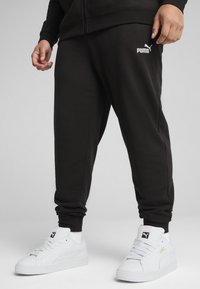 Pantaloni della tuta neri con caviglia a costringere, con logo Puma bianco. Abbinati a sneaker Puma bianche, con tomaia in pelle testurizzata.