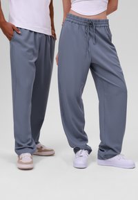 Pantalons détendus à rayures grises avec une taille élastique et un cordon de serrage, associés à des baskets décontractées. Texture lisse et jambes larges.