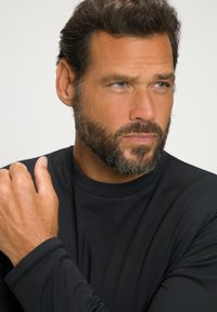 Sort langærmet shirt med rund halsudskæring, glat tekstur og minimale syninger. Modellen har skæg og kort hår.