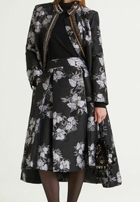 Veste florale noire avec accents en chaîne argentée, assortie à une jupe florale noire. Tissu lisse avec plis structurés. Sac à main noir.