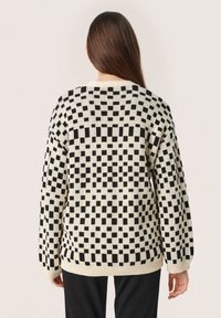 Stickad tröja med ett svart-vitt rutmönster, avslappnad passform, ribbad mudd och nederkant, designad med rund halsringning.