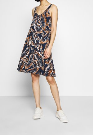 Robe florale marine avec des motifs tropicaux orange et blanc, coupe ample, bretelles spaghetti et longueur genou, assortie à des baskets blanches.