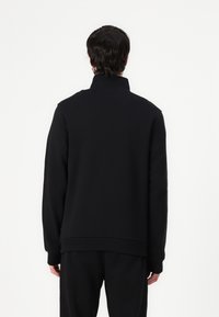 Sudadera negra con cuello alto, mangas largas y puños acanalados. Textura suave con corte recto y sin logotipos ni patrones visibles.