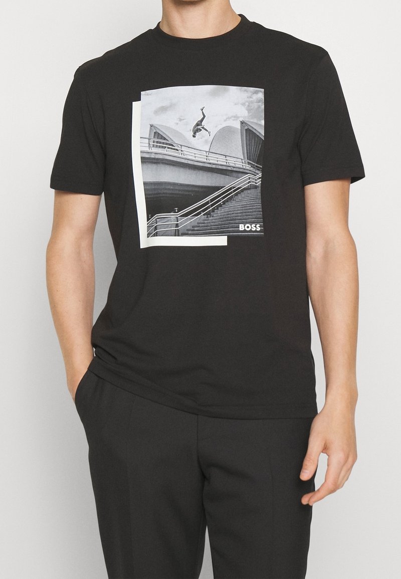 T-shirt en coton noir avec un grand graphique en noir et blanc d'un skateur sur des escaliers, encadré par un rectangle blanc avec le texte "BOSS".