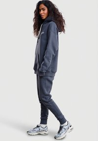 Pohodlná tmavě šedá mikina s kapucí a přední kapsou, shodné tepláky a reflexivní stříbrné tenisky. Měkká látka, volný střih.