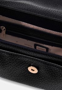 Zwarte tas van gestructureerd leer met een binnenvak met rits en merklogo, benadrukt door een drukknoopsluiting in goudkleur en een beige voering.