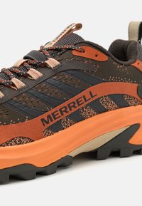 Buty outdoorowe Merrell w ciemno-brązowym i pomarańczowym wzorze, z siateczkową cholewką, gumową podeszwą z wyraźnymi bieżnikami i teksturowanym wykończeniem.