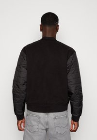 Zwarte bomberjack met een gestructureerd fleece lichaam, gevoerde nylon mouwen, geribde manchetten en tailleband, met een minimalistisch ontwerp.