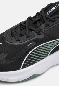 Chaussure de sport noire avec un dessus texturé et des détails en mesh. Présente une semelle intermédiaire blanche et un accent rayé vert sur la semelle extérieure. Inclut du PWR tape.