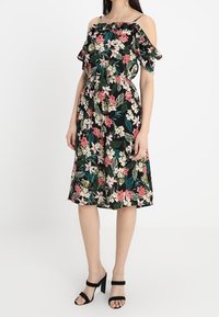 Květinové šaty bez ramínek s volánkovými rukávy; mají přiléhavý pas, sukně délky ke kolenům a černé pozadí s růžovými a zelenými květy.