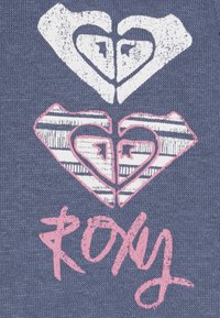 Il tessuto blu presenta forme stilizzate di cuori e diamanti in bianco e rosa. "Roxy" è stampato in rosa con un carattere corsivo nella parte inferiore.