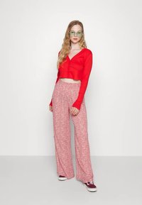 Top vermelho curto de manga longa com botões; calças largas cor-de-rosa com padrão fluido; combinado com óculos de sol verdes e ténis cor de vinho.