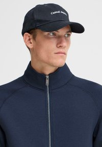 Navy zip-up jacket with a high collar and raglan sleeves, paired with a navy cap featuring "Casual Apparel" in white text.