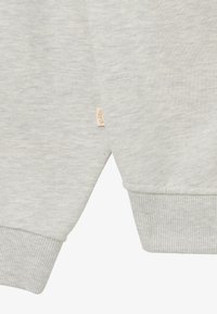 Sudadera gris claro con puños y dobladillo acanalados. Textura suave con un sutil patrón jaspeado. Pequeña etiqueta de la marca visible cerca de la costura.