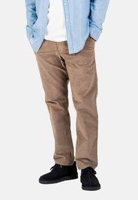 Braune Cordhosen mit geraden Beinen, Taschen vorne und einer glatten Textur, kombiniert mit schwarzen Knöchelschuhen und einem hellblauen Hemd mit Knöpfen.