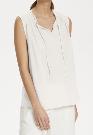 Blusa bianca senza maniche con una finitura testurizzata, rifinitura in pizzo all'escella e vestibilità rilassata. Cordini nel dettaglio del collo.