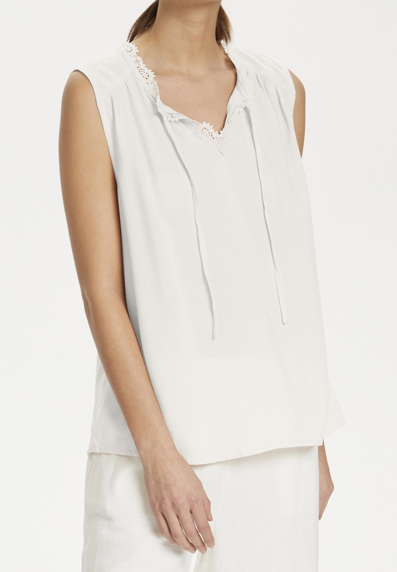 Blusa bianca senza maniche con una finitura testurizzata, rifinitura in pizzo all'escella e vestibilità rilassata. Cordini nel dettaglio del collo.