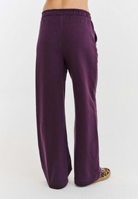 Fialové kalhoty širokého střihu s uvolněným střihem, elastickým pasem a měkkou texturou. Výrazným detailem jsou elegantní boční švy a minimalistický design.