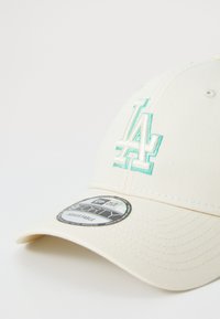 Kremfarget baseballcap med turkise broderte "LA" logo, buet skygge og justerbar stropp. Inkluderer en etikett som sier "9FORTY."