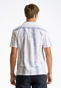 Camisa de botón de manga corta hecha de tela blanca, con patrones geométricos azules y un cuello estándar. La vista trasera muestra los detalles de costura.