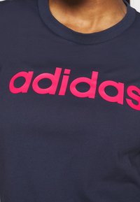 Mörkblå t-shirt i bomull med rund halsringning; har en framträdande rosa "adidas"-logotyp över bröstet.