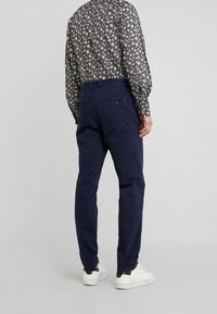 Mörkblå bomullbyxor med rak passform, utrustade med två bakfickor, stylade med en mönstrad skjorta med långa ärmar och vita sneakers.