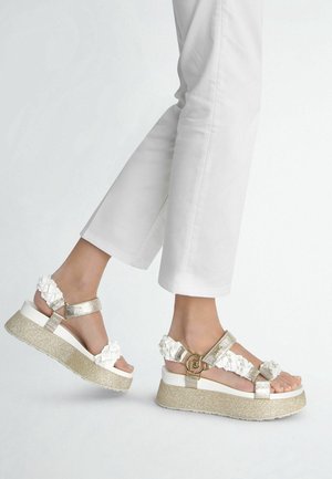 Sandales à plateforme dorées et blanches avec accents floraux texturés, brides argentées et base pailletée. Design minimaliste avec boucles réglables.