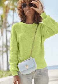 Limegrüner Strickpullover mit übergroßen Ärmeln, kombiniert mit einer kleinen blauen geflochtenen Handtasche mit einer goldenen Kette und einem runden Verschluss.