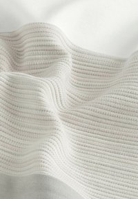 Tissu texturé avec des rayures gris clair et blanc cassé. Matériau doux avec un aspect ondulé, mettant en valeur le motif tissé et les plis délicats.