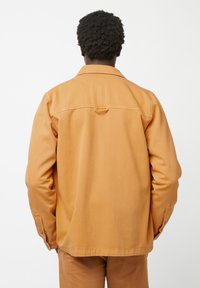 Orange Denimjacke mit regulärem Kragen, Knopfmanschetten und Rückenpasse. Glatte Textur und gerader Schnitt.