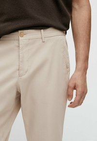 Beige chino's met een rechte pasvorm, voorzien van een knoopsluiting, zijzakken en een gladde textuur. De tailleband is plat met riemlussen.