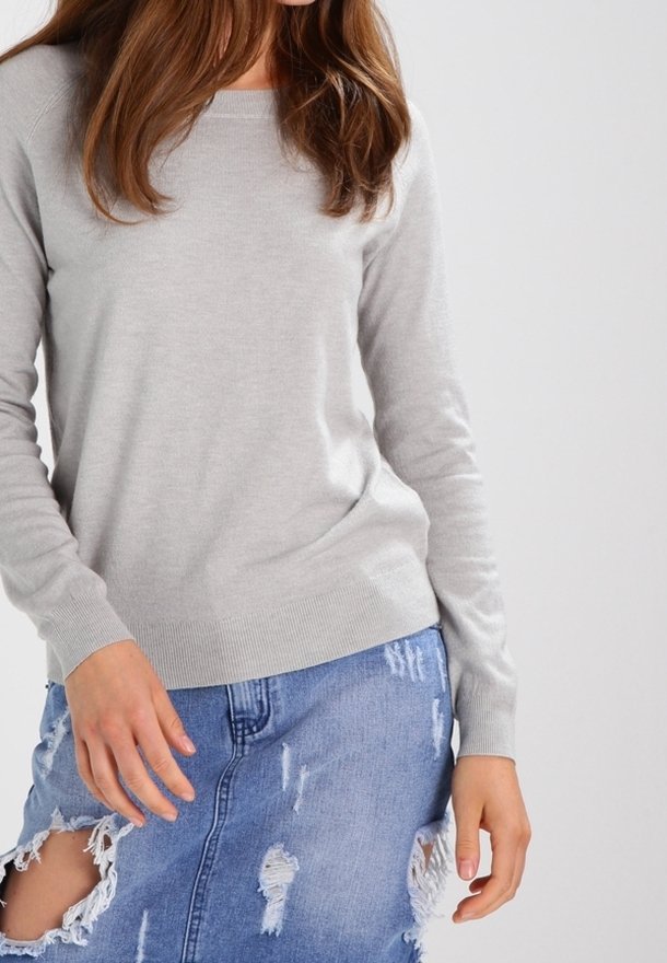Femme portant un pull léger à manches longues gris clair et une jupe en jean bleu délavé avec de grandes déchirures.