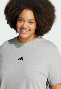 Light gray cotton t-shirt featuring a black Adidas logo on the chest, with a crew neckline and short sleeves. Soft, casual fabric texture.