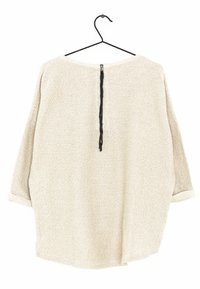 Jasnobeżowy, luźny sweter o teksturowanym splotcie, z rękawami o długości trzech czwartek i zamkiem błyskawicznym z tyłu, powieszony na czarnym wieszaku.