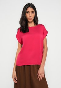 Różowy bluzka z krótkim rękawem z gładkiej tkaniny z prostym, okrągłym dekoltem, połączona z brązową, fakturowaną spódnicą o rozkloszowanym kroju.