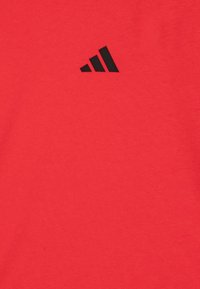 Rotes Baumwoll-T-Shirt mit einem schwarzen adidas-Logo auf der linken Brust. Glatte Textur, Rundhalsausschnitt-Design. Leichter und atmungsaktiver Stoff.