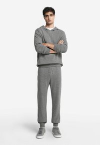 Grå huvtröja och matchande sweatpants med avslappnad passform, ribbade ärmslut och dragsko i midjan. I kombination med grå sneakers.